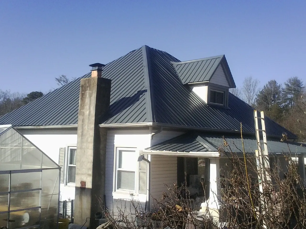 Dark blue standing seam metal roof on a white farmhouse with dormer — Slate & Tile Roof Repair by Roofing Brothers in Sixes