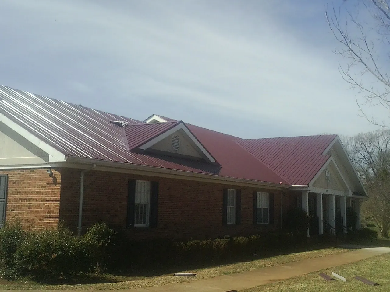 Red metal roof with gabled entries on a long brick building, from a Hail Damage Roof Repair job in Sixes
