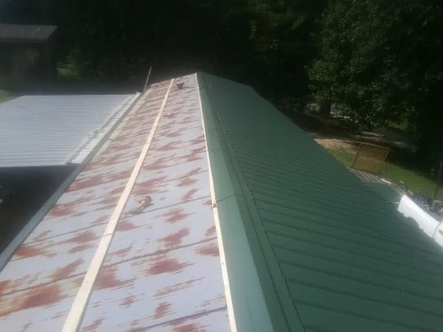 Old rusted panels beside newly installed green metal roofing — Wind Damage Roof Repair by Roofing Brothers in Sixes