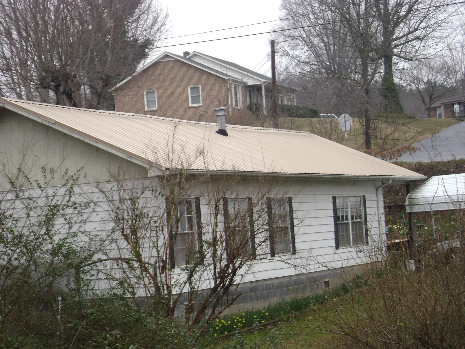 Tan metal roof on a white sided house set into a hillside — Commercial Roofing by Roofing Brothers in Sixes