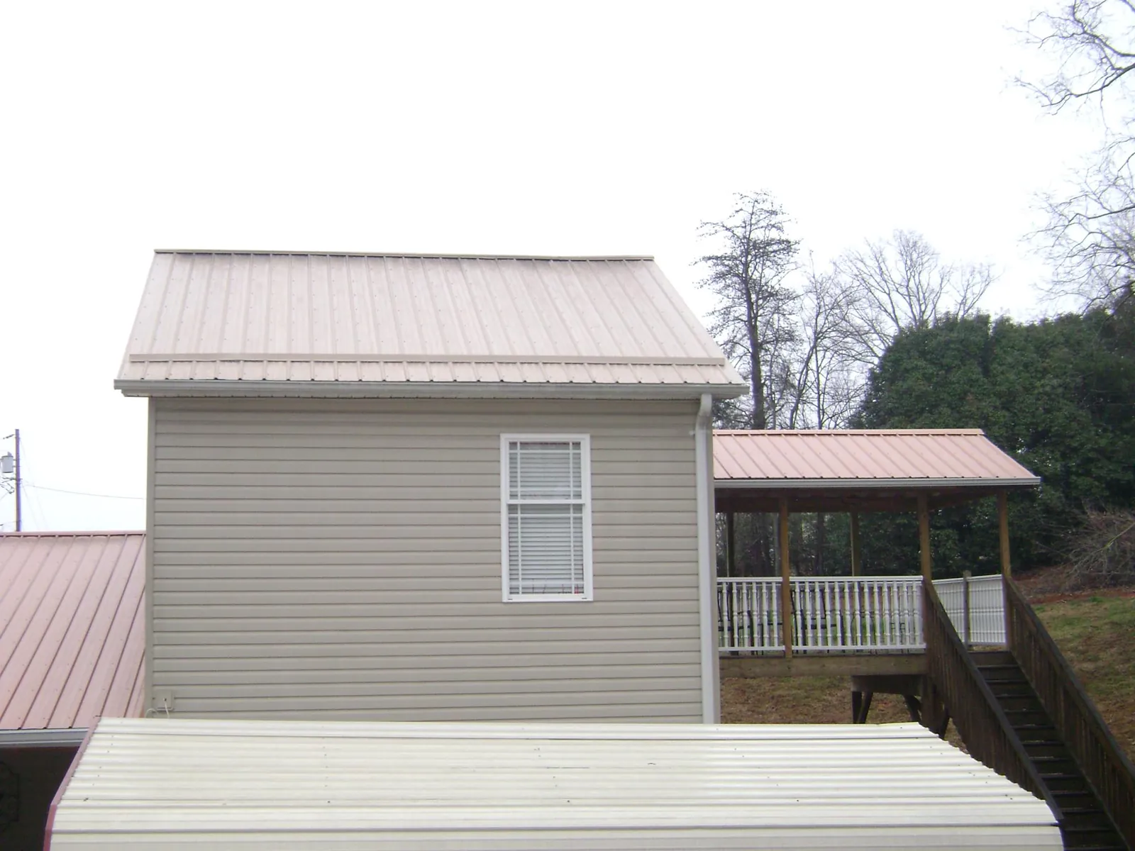 Tan metal roofs on a two story addition and attached porch, from a Roof Replacement job in Sixes